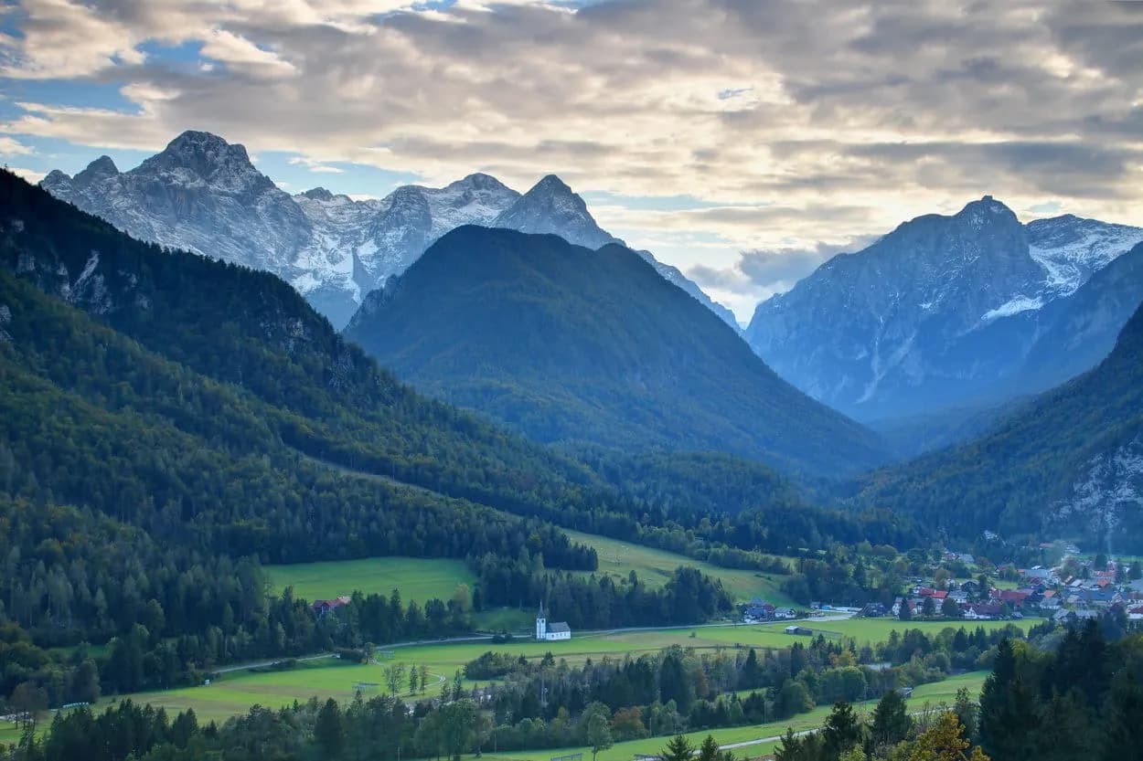 Evening view of Slovenian mountains, valley, and Mojstrana village with a small white church.