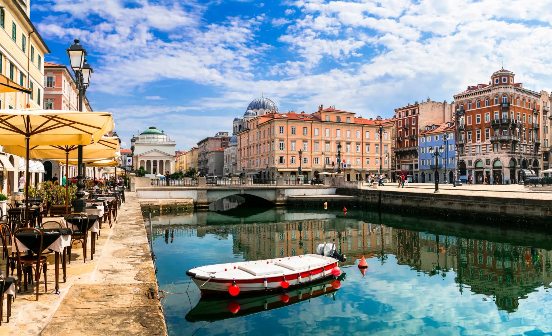 Small boat moored in canal reflecting colorful historic buildings and blue sky.