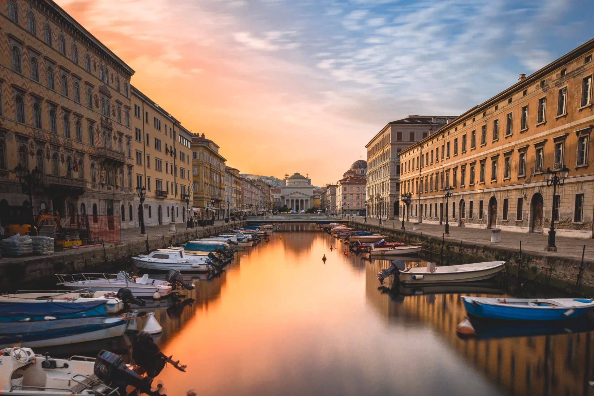 Boats moored in canal between historic buildings at sunrise or sunset