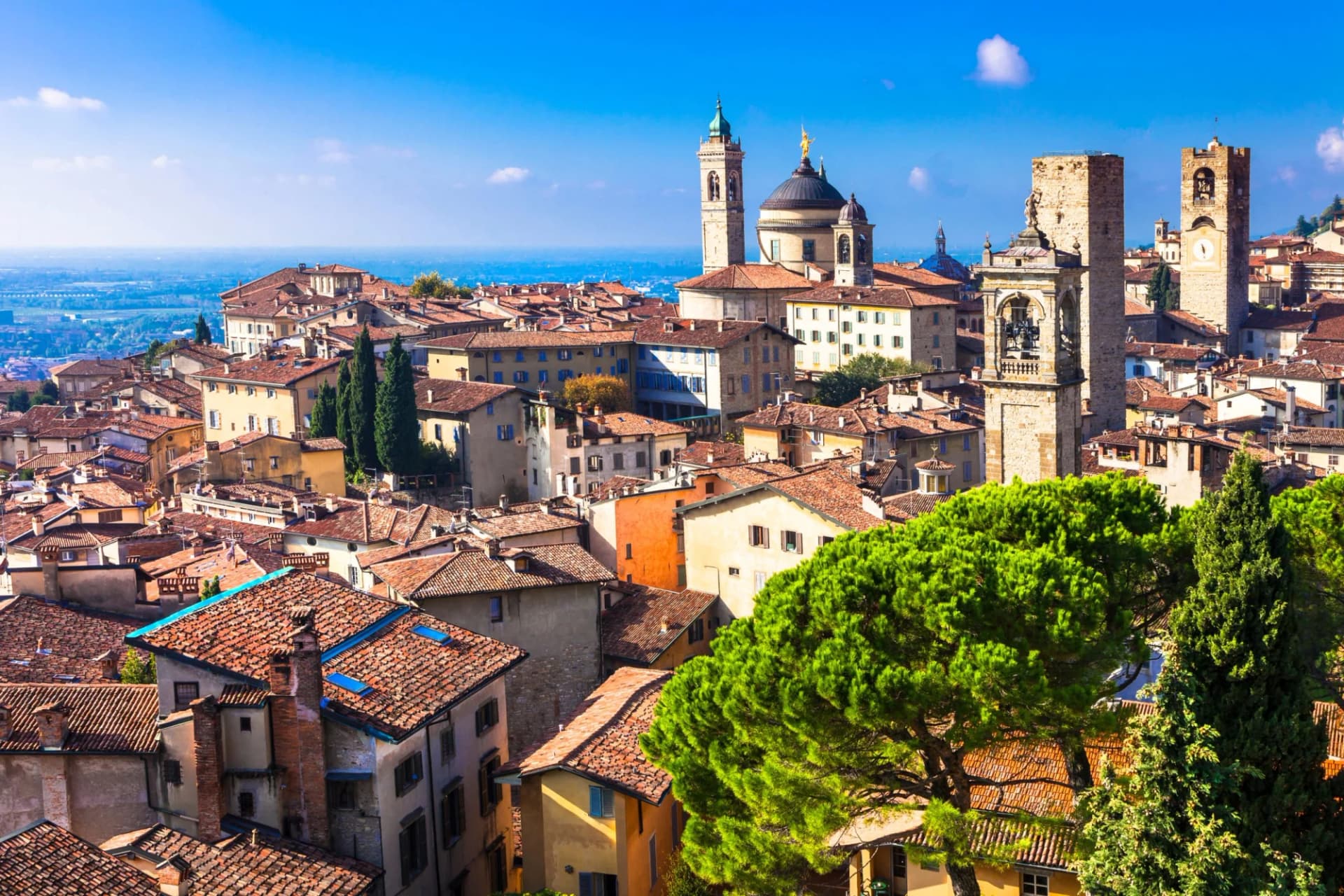 Rooftops of historic Bergamo city with towers and domes under a bright blue sky.