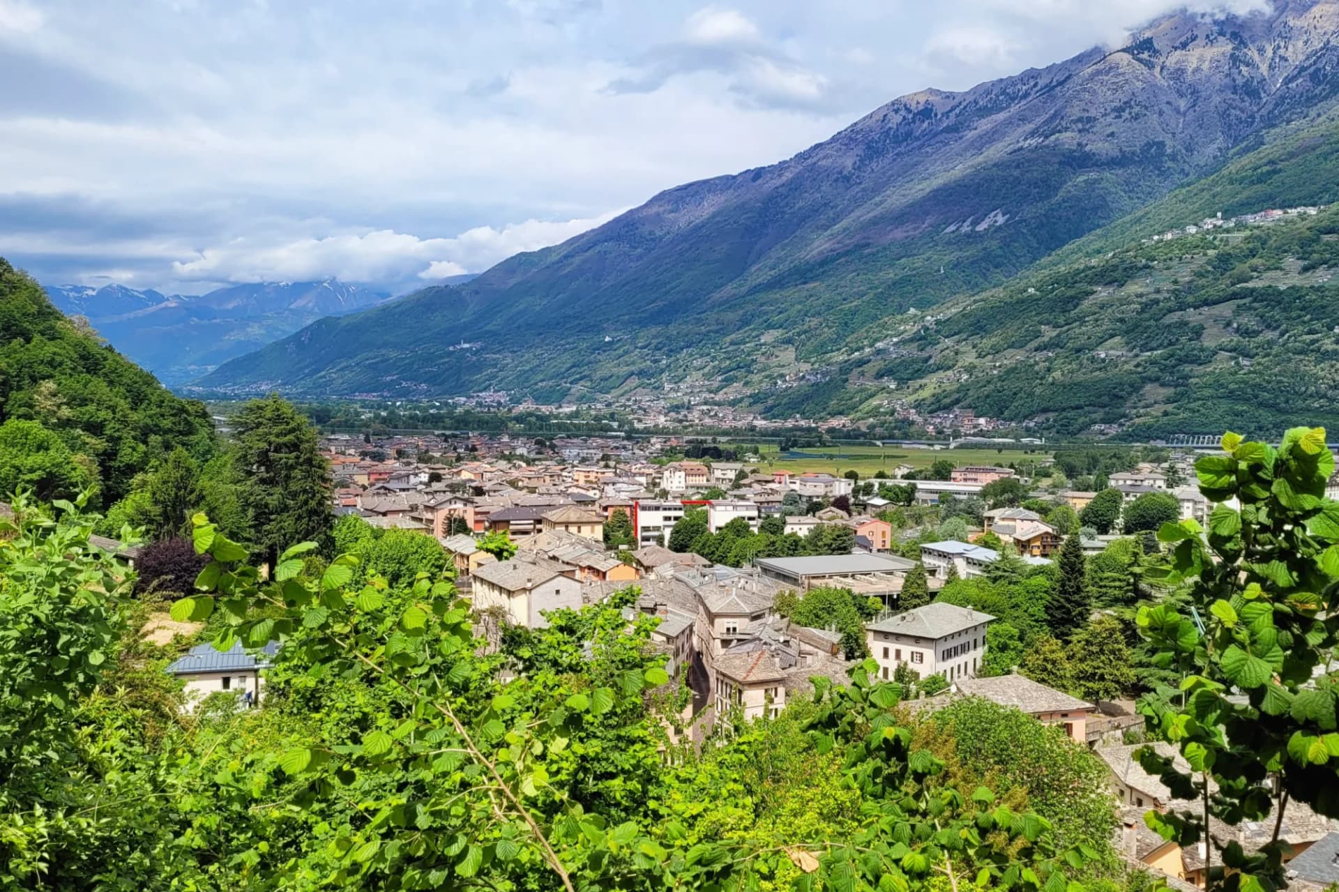 Town of Morbegno in Valtellina valley with steep green mountains under cloudy sky.