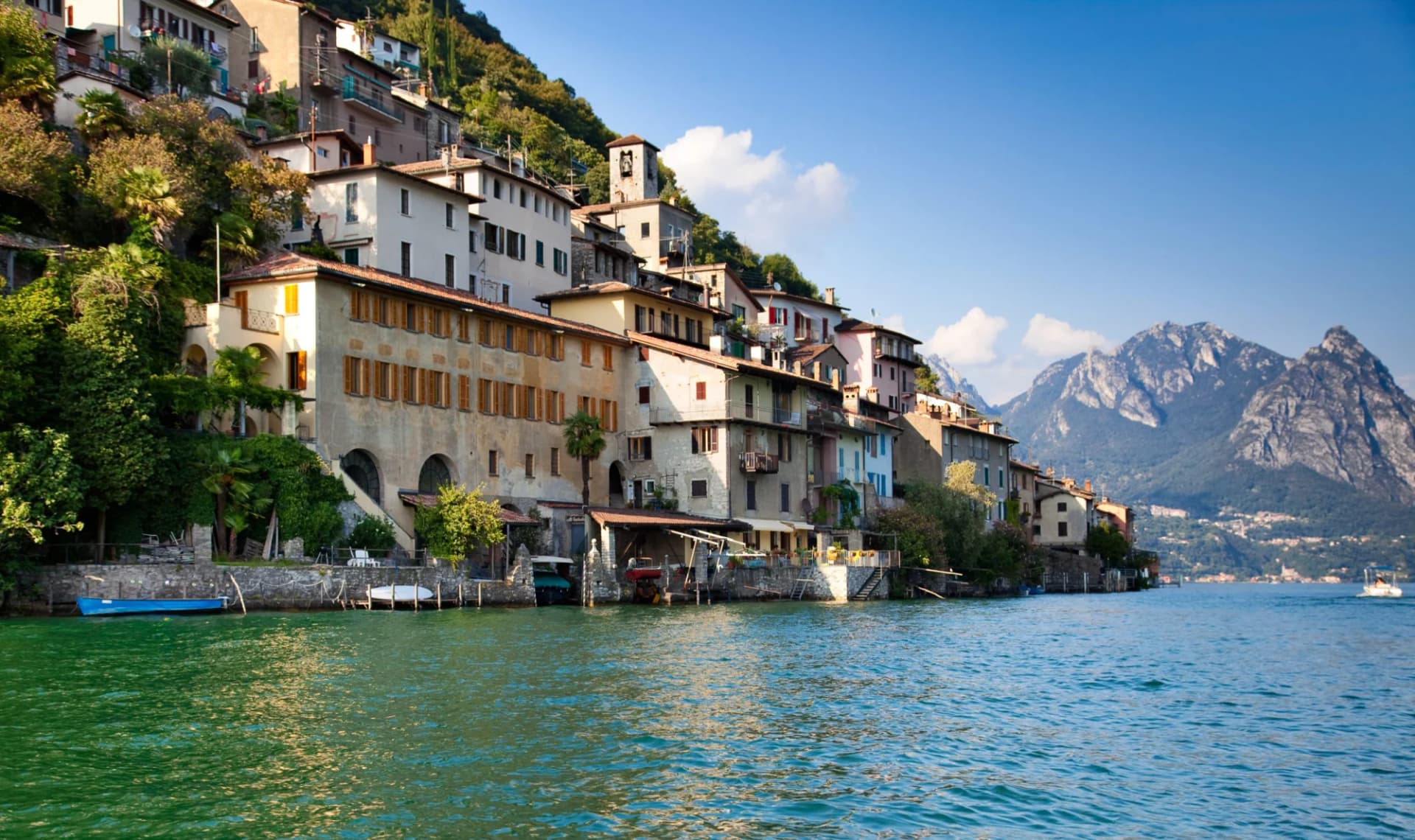 Houses built on a steep hillside above a lake with mountains in the background, Lake Lugano.