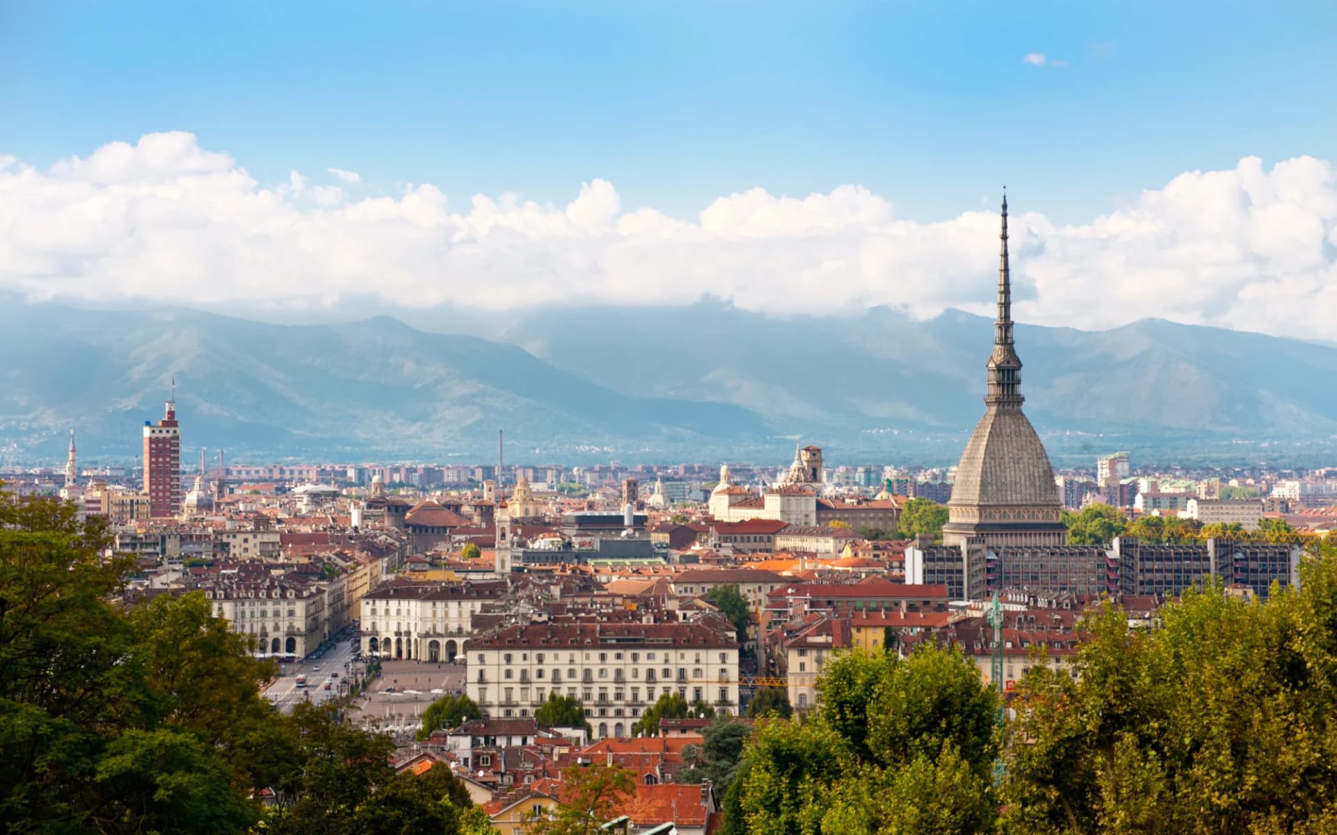 Cityscape of Turin with Mole Antonelliana and mountains under a blue sky.