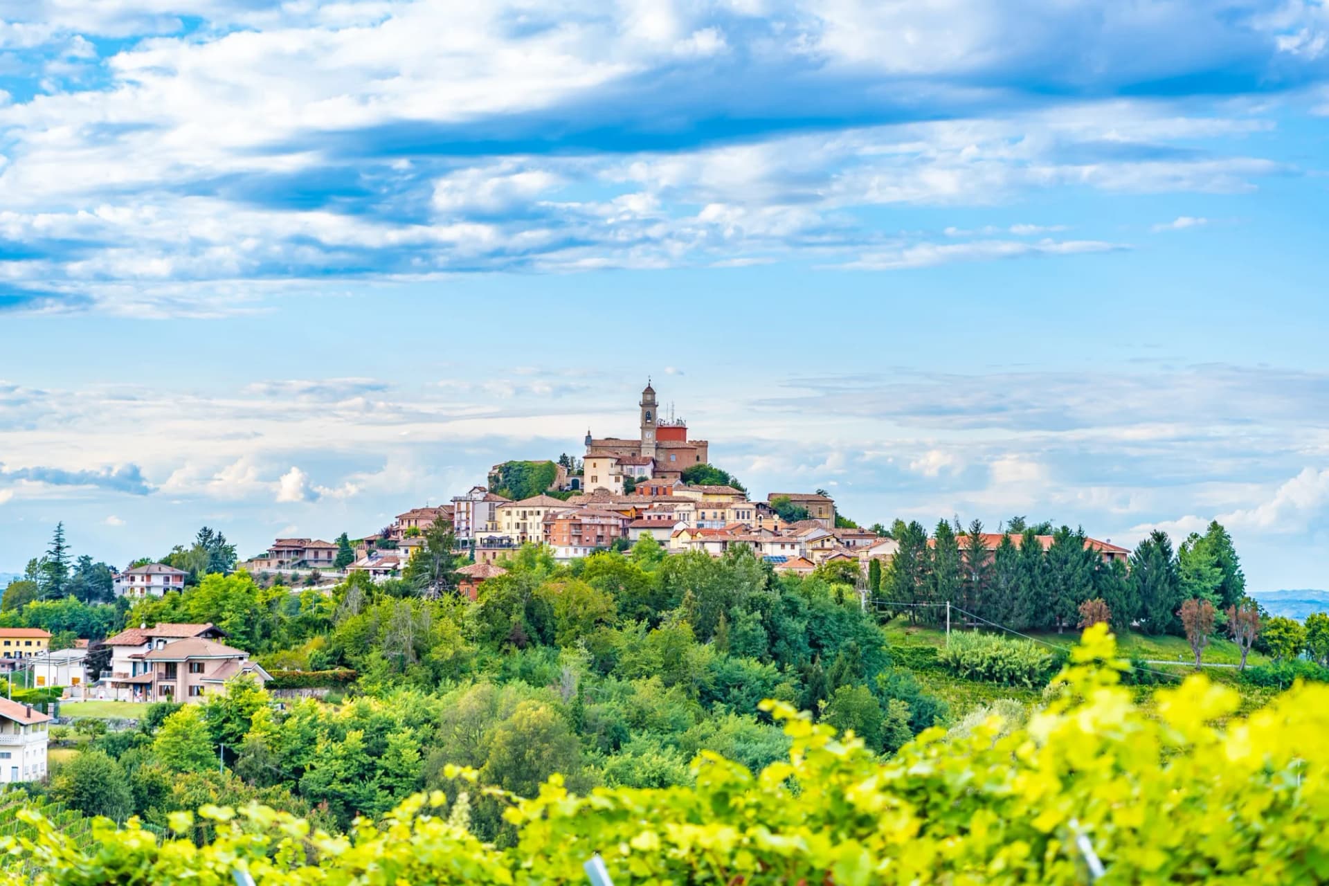Hilltop town of Calosso Costigliole d'Asti, Piedmont, Italy, above green vineyards under blue sky.