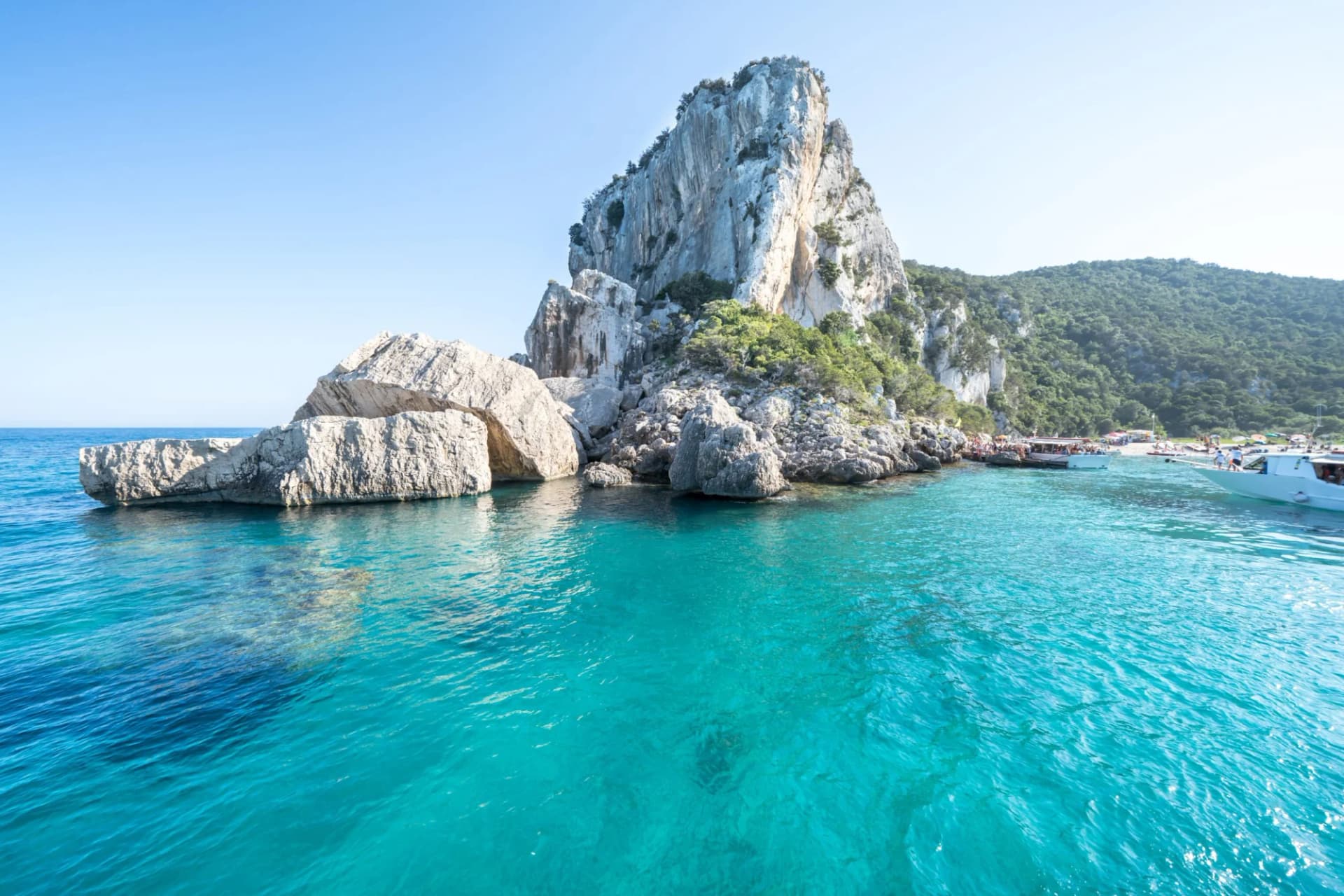 Turquoise water near massive white cliffs and lush green hillside with boats docked.