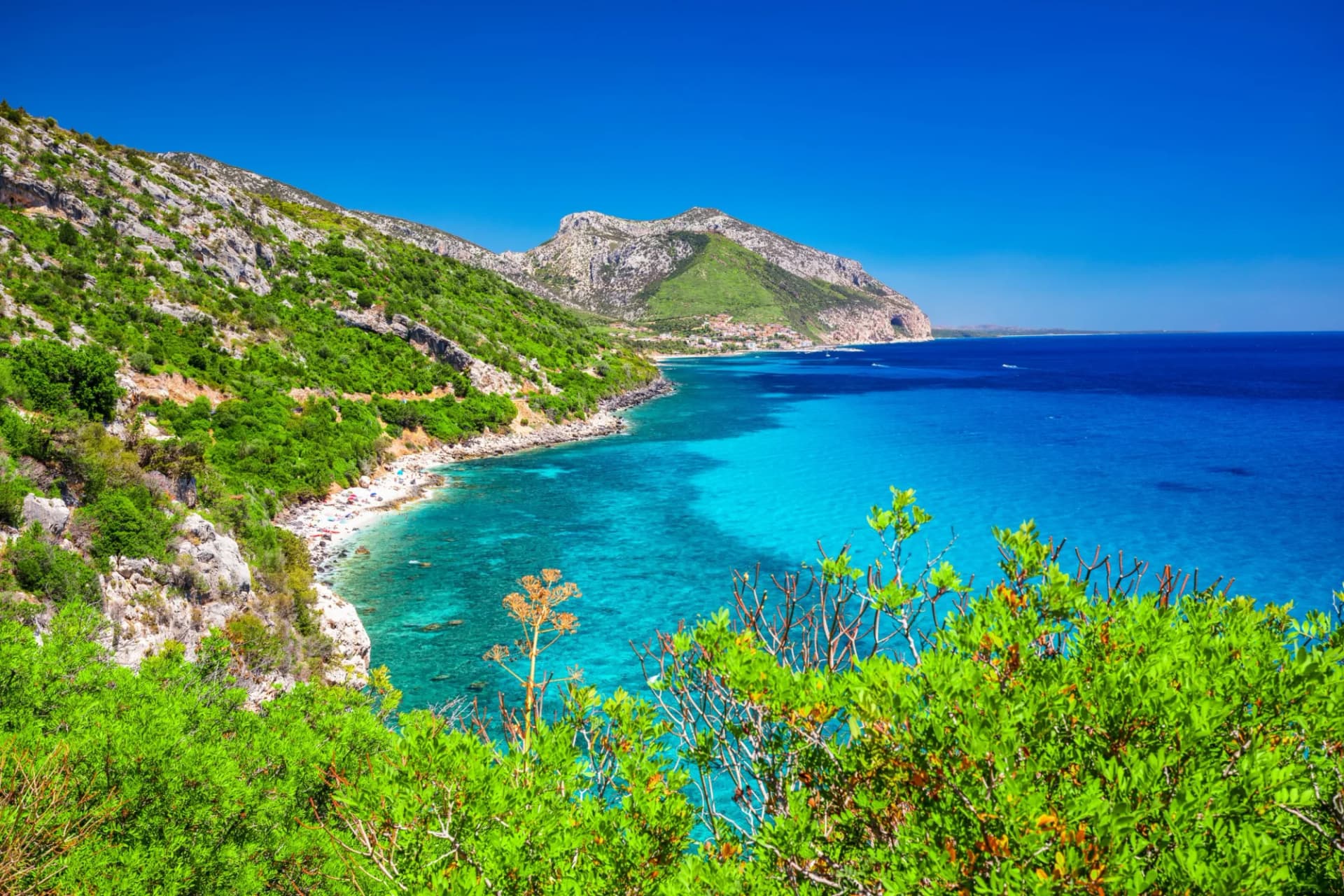 Coastal view of Cala Gonone with lush green hills, turquoise sea, and a small beach.