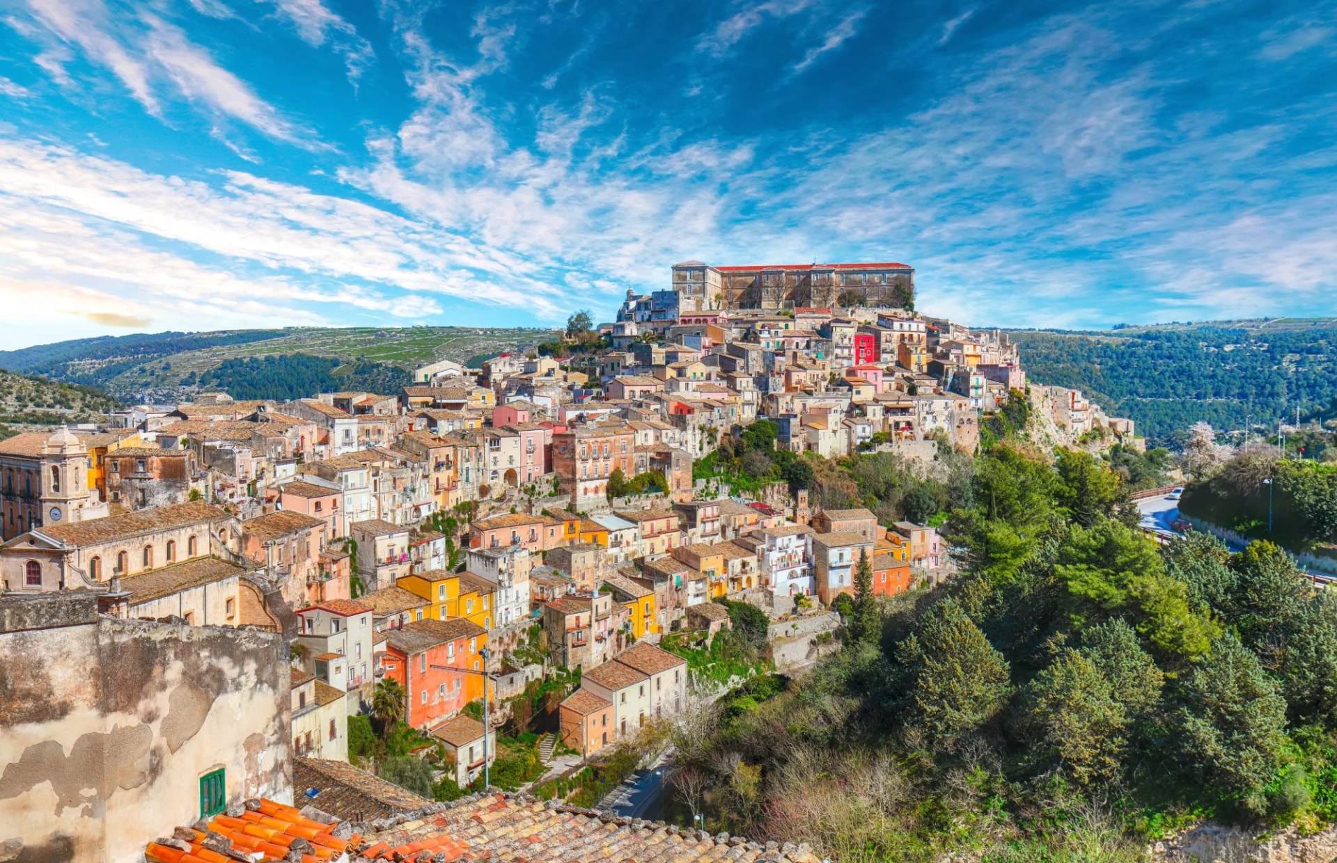 Sunny Ragusa cityscape with Palazzo Cosentini and Duomo di San Giorgio church on hill.