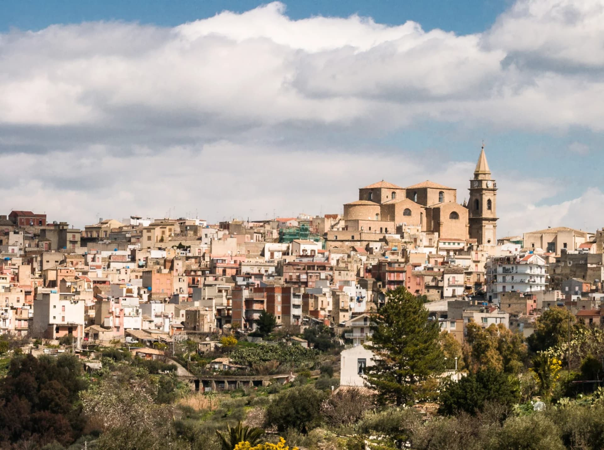 Hillside town with dense buildings and a prominent church tower under a cloudy sky.