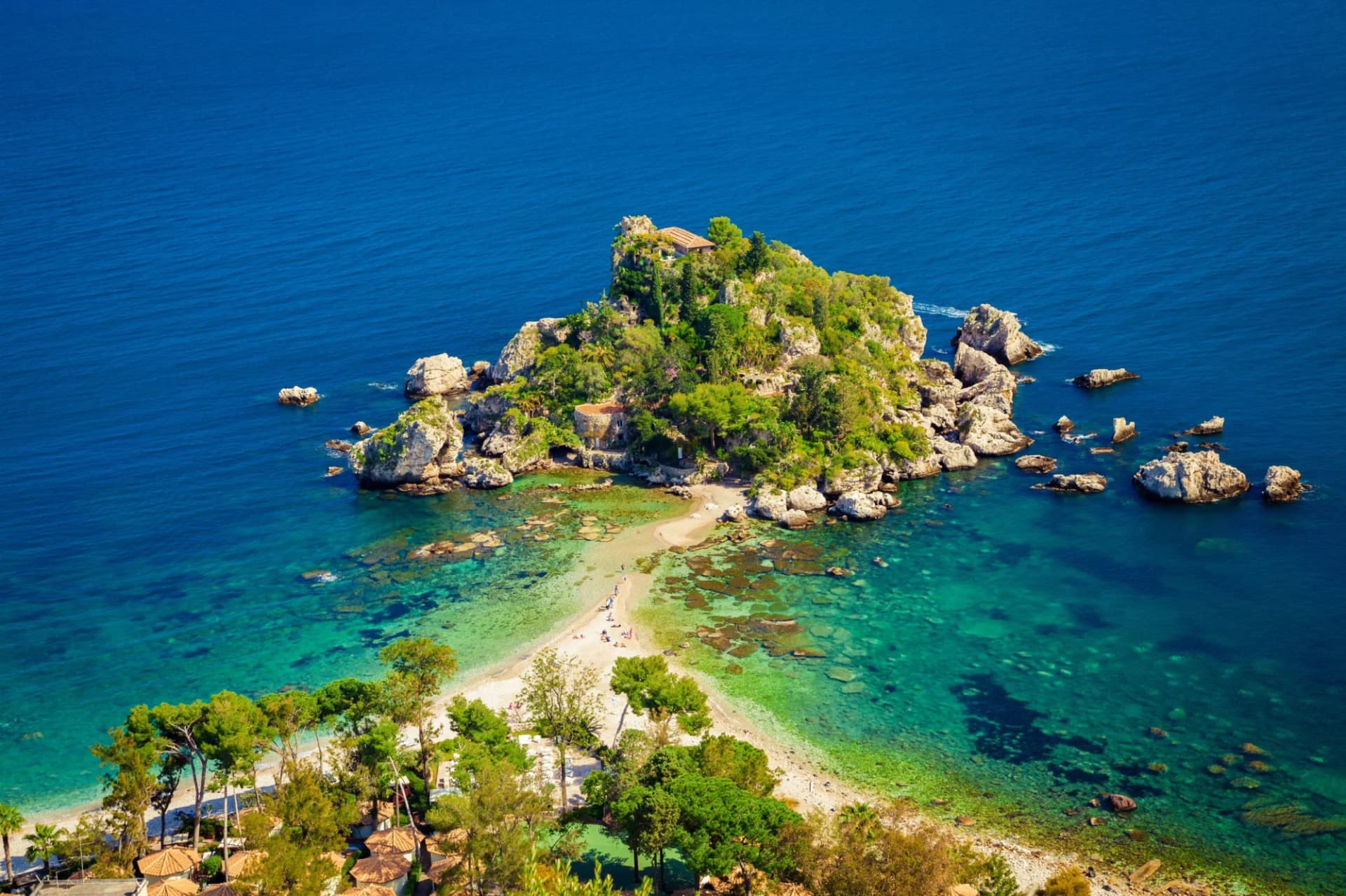 Isola Bella connected to shore by a sand spit, surrounded by turquoise and deep blue Mediterranean sea.