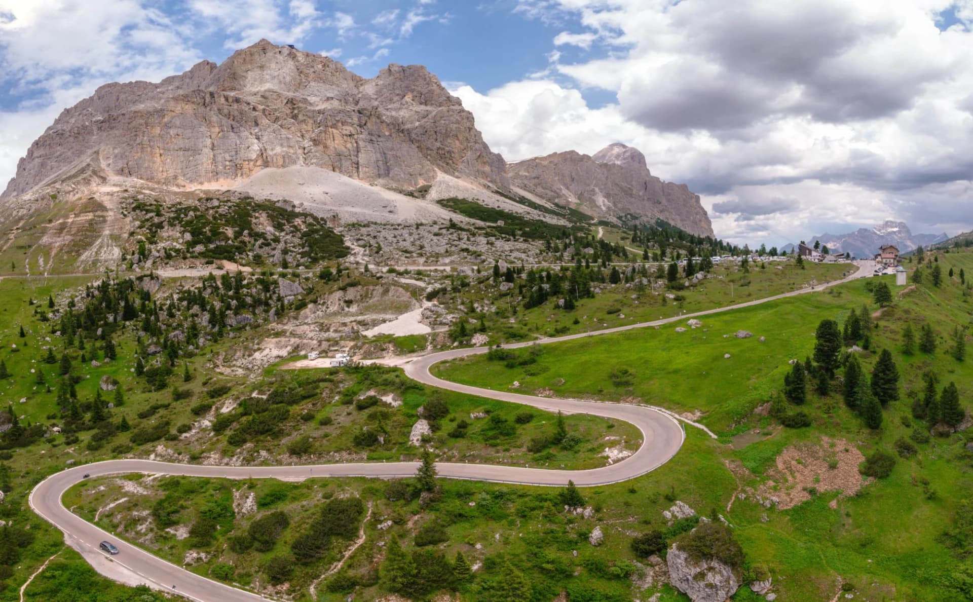 Winding mountain road at Falzarego Pass, Dolomites, Italy, surrounded by green slopes and rocky peaks.