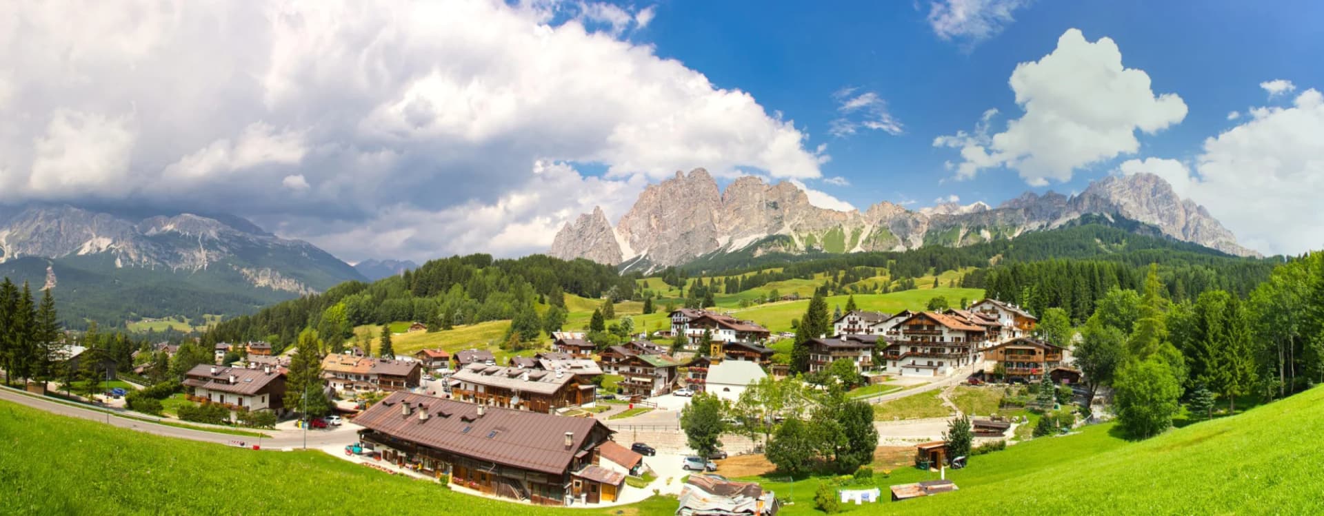 Alpine resort town in the Dolomites of Italy with green meadows and rugged mountains.