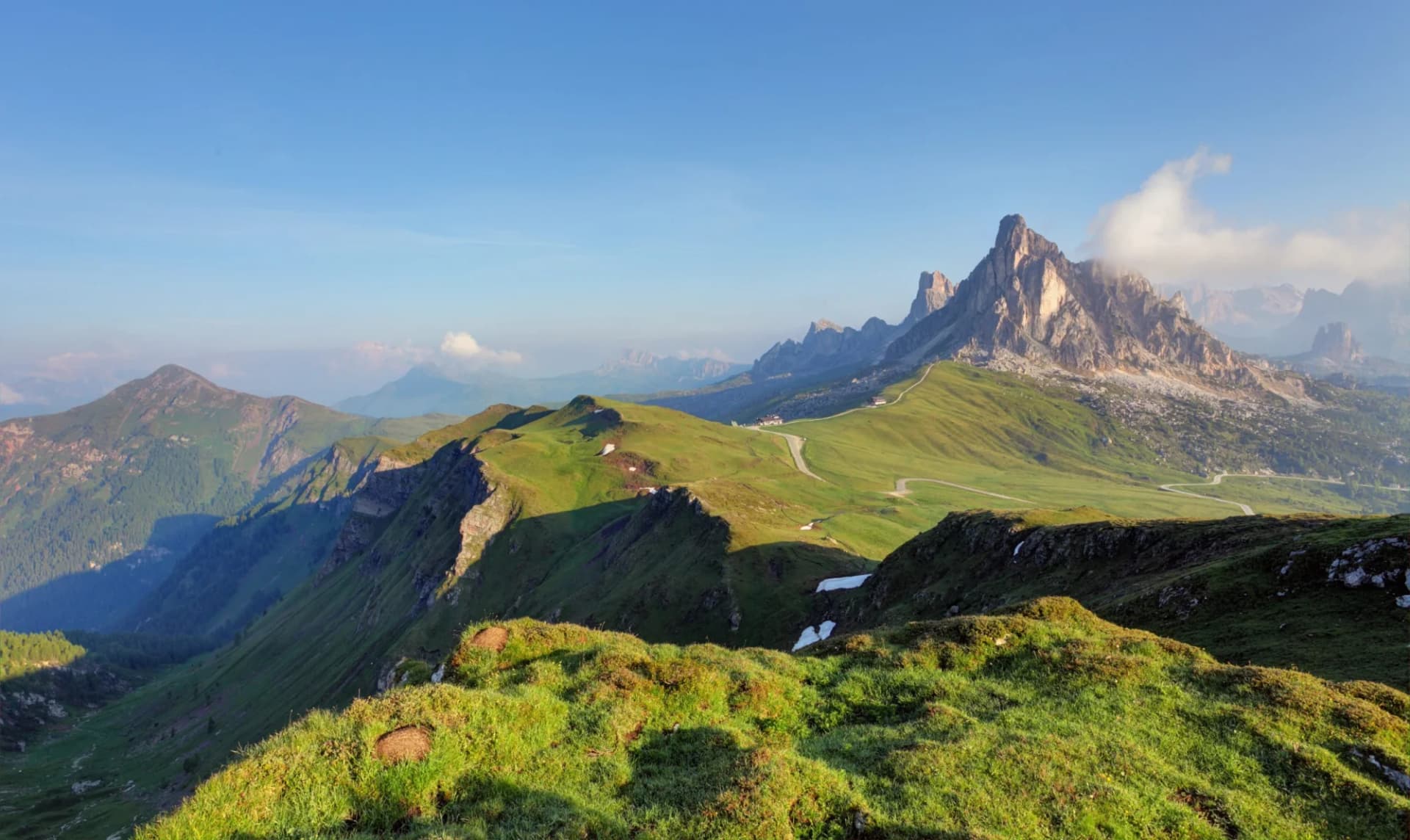 Mountain panorama of the Dolomites from Passo di Giau with green slopes and winding road.