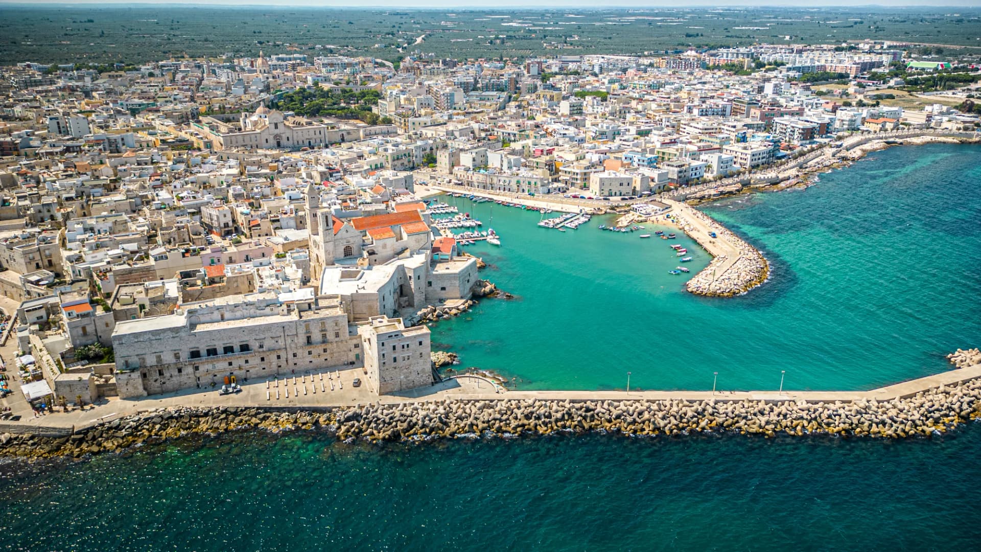 Panoramic view of Giovinazzo's ancient village and harbor in Puglia with turquoise Mediterranean water.