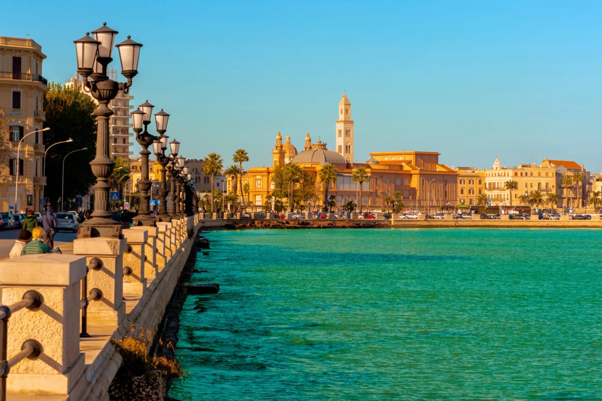 Panoramic view of Bari seafront with historic buildings and Basilica San Nicola across turquoise water.