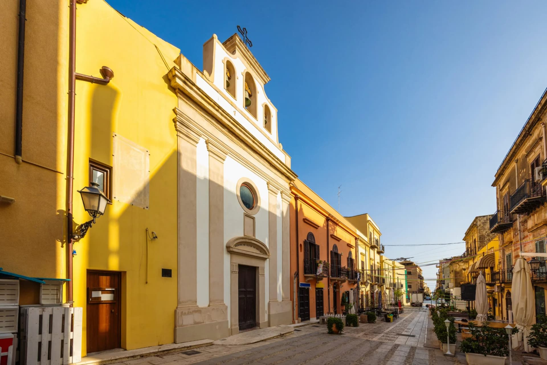 Street in Castellammare del Golfo with church and colorful buildings in morning light, Sicily.