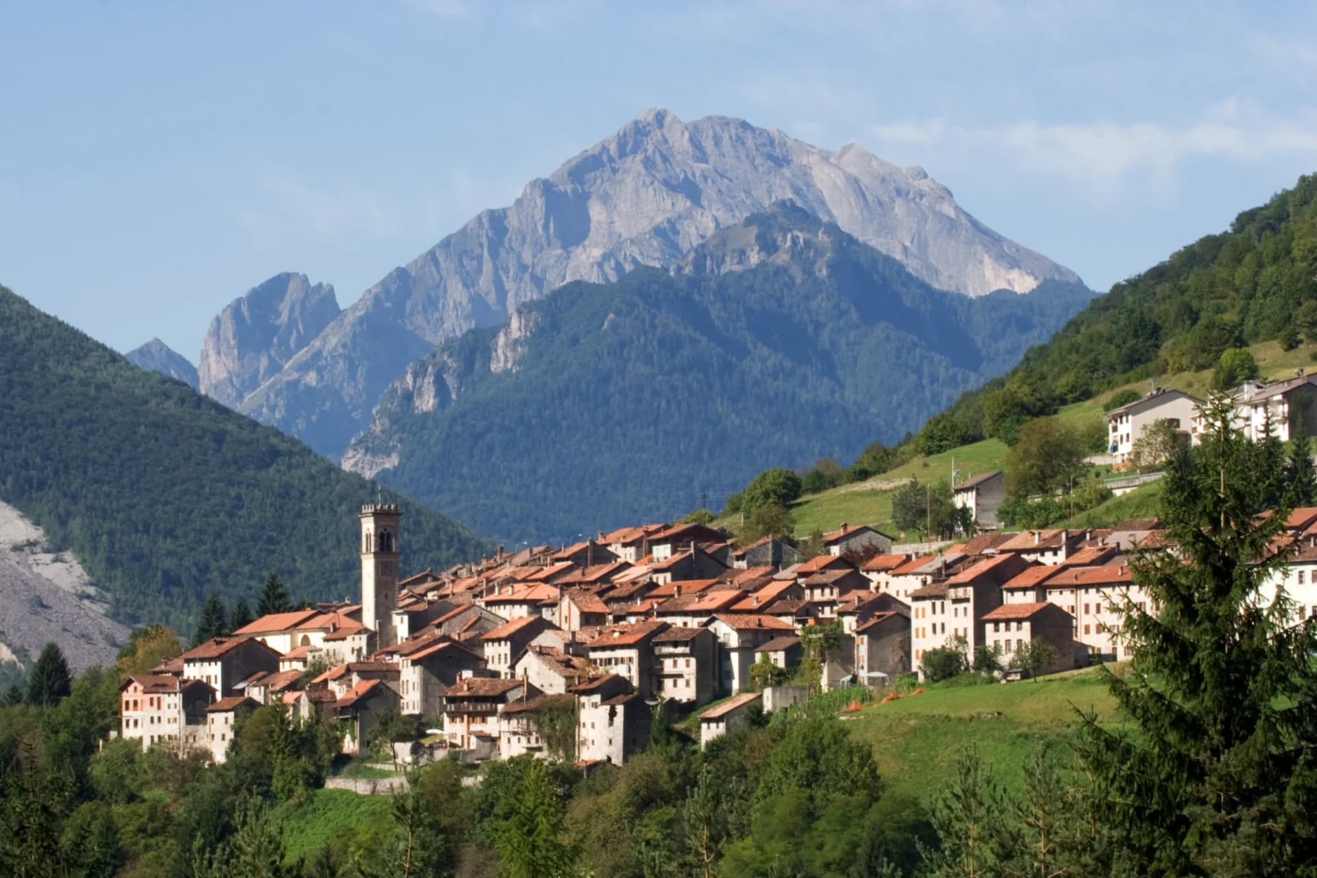 Alpine village with terracotta roofs nestled below a large, rocky mountain peak in Longarone.