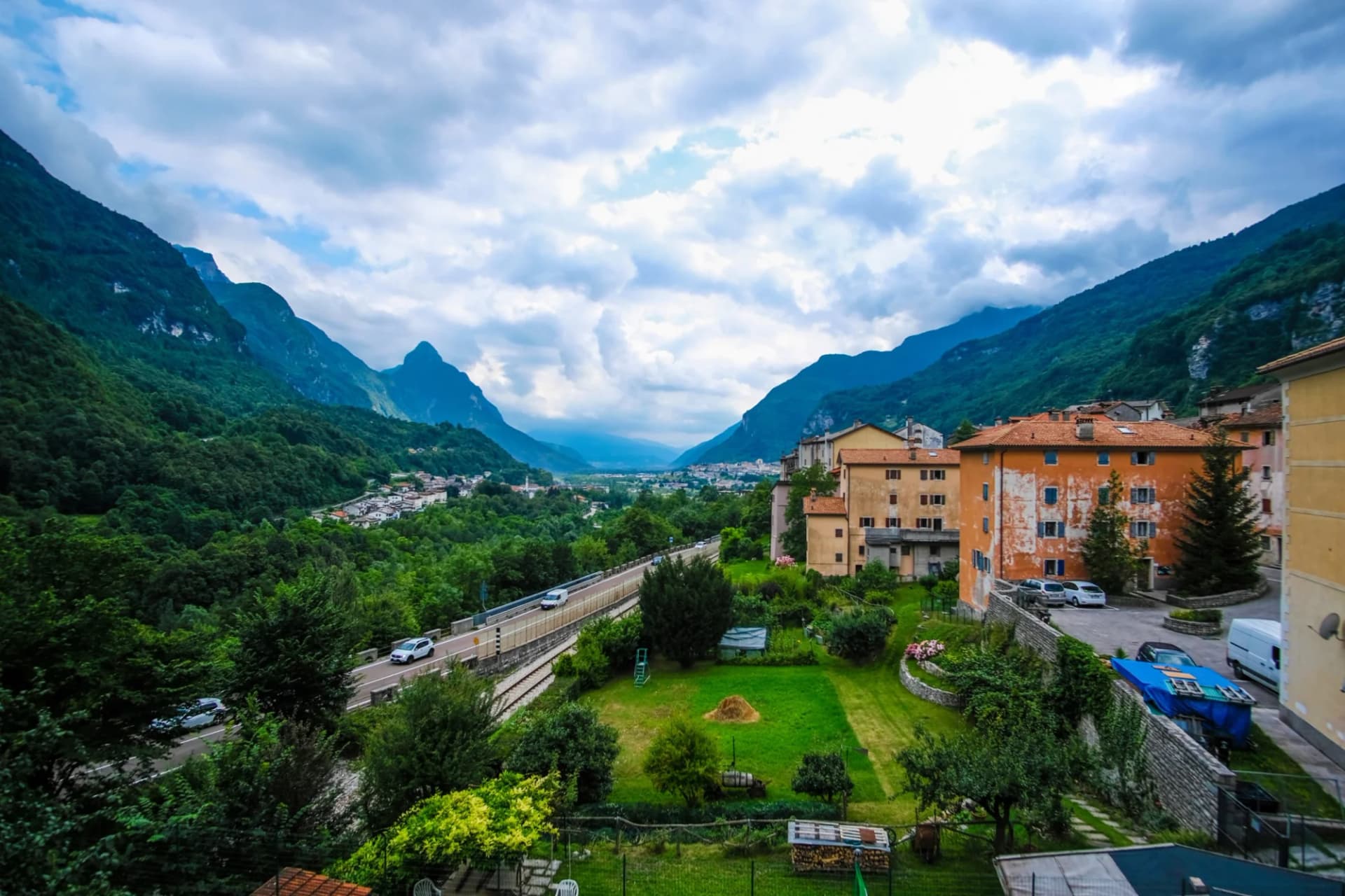 Alpine village with colorful buildings nestled in a valley surrounded by steep, forested mountains under a cloudy sky.