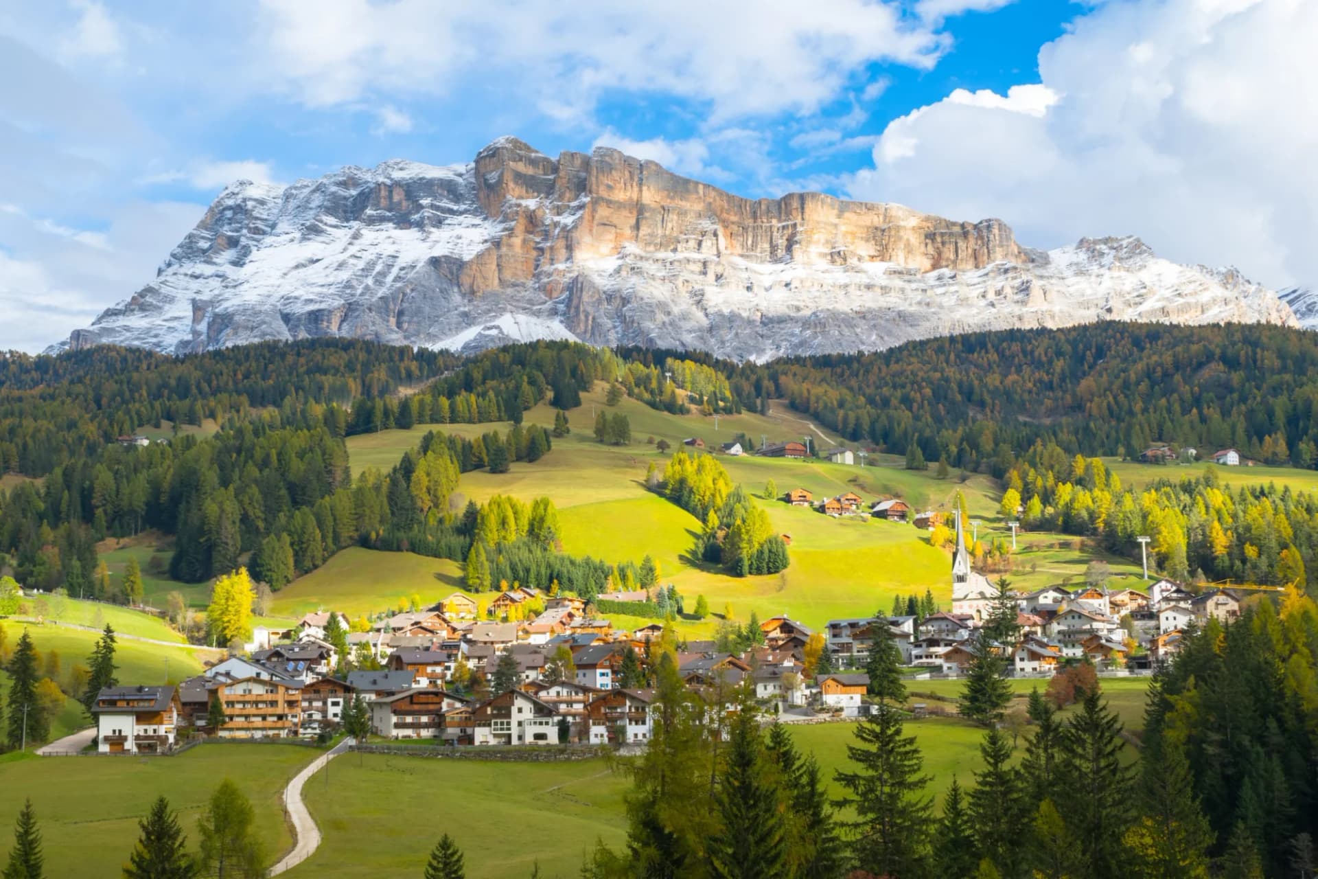 Alpine village nestled in green valley below snow-capped mountains, Alta Badia.