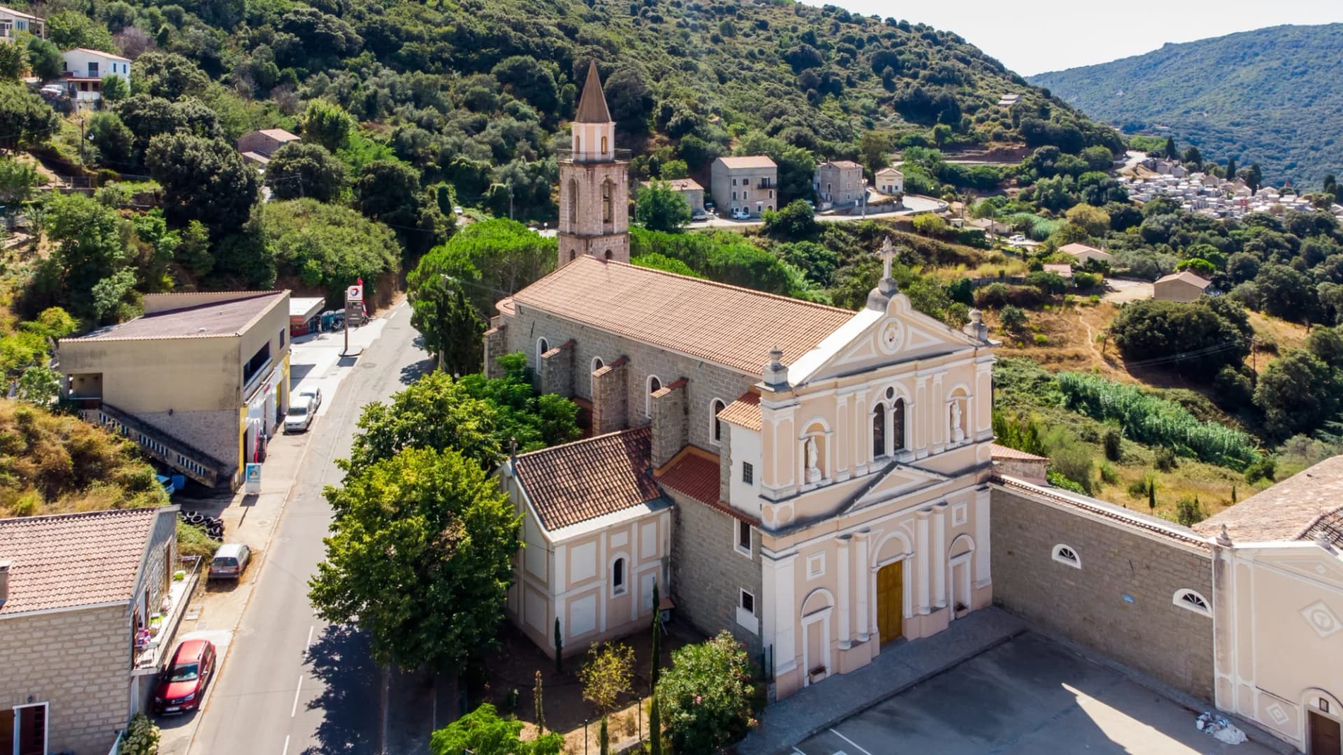 Aerial view of Saints Cosimo and Damian Convent in Sartene, Corsica, nestled in green mountains.