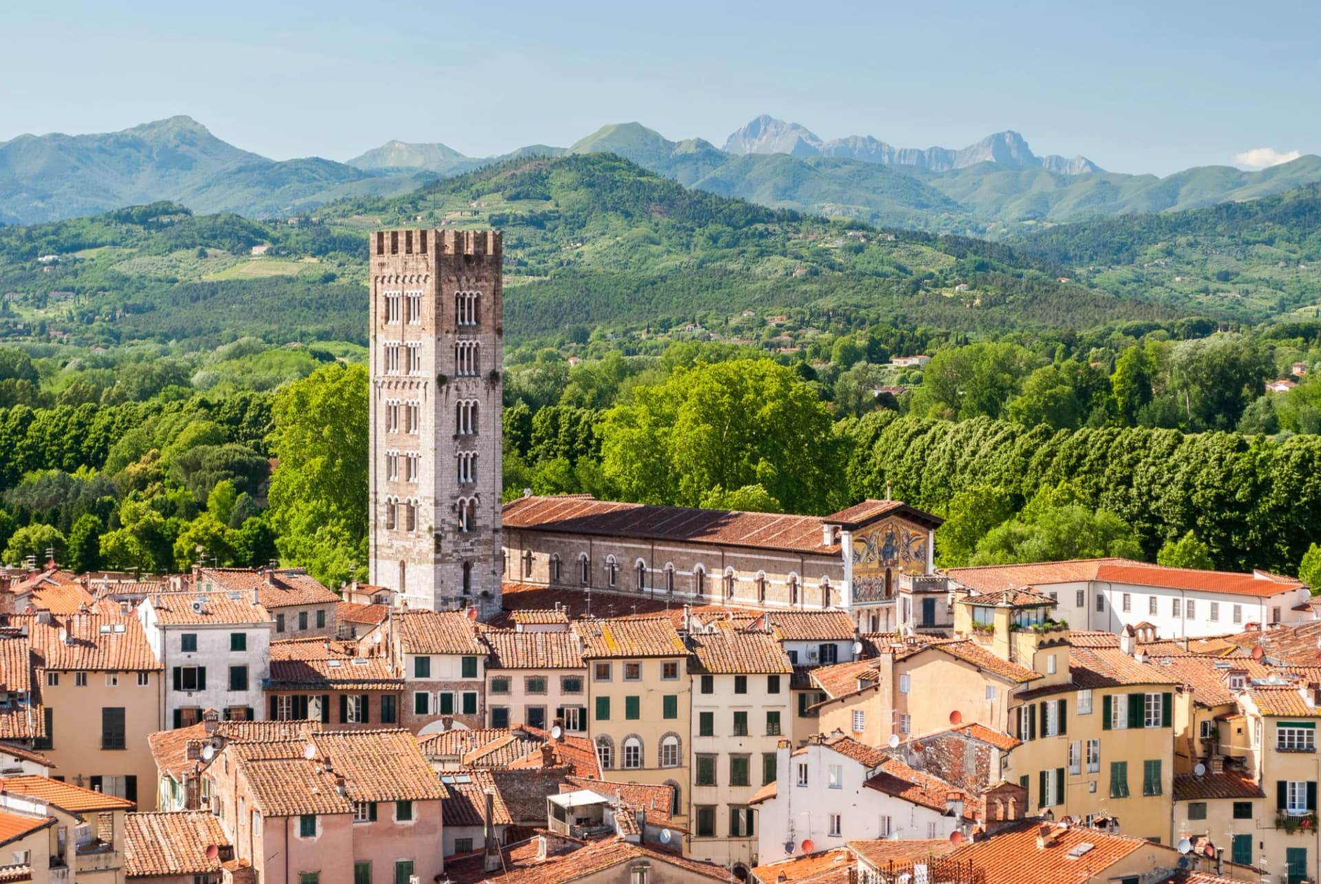 Lucca city rooftops with medieval tower and green mountains in background, Italy