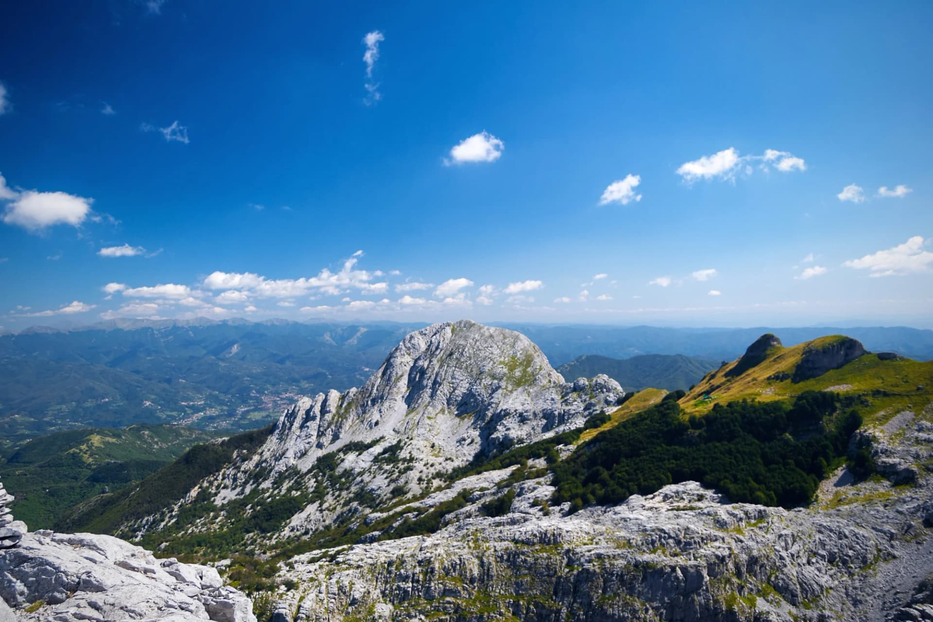 Rugged limestone mountains under a bright blue sky with scattered white clouds, Apuan Alps.
