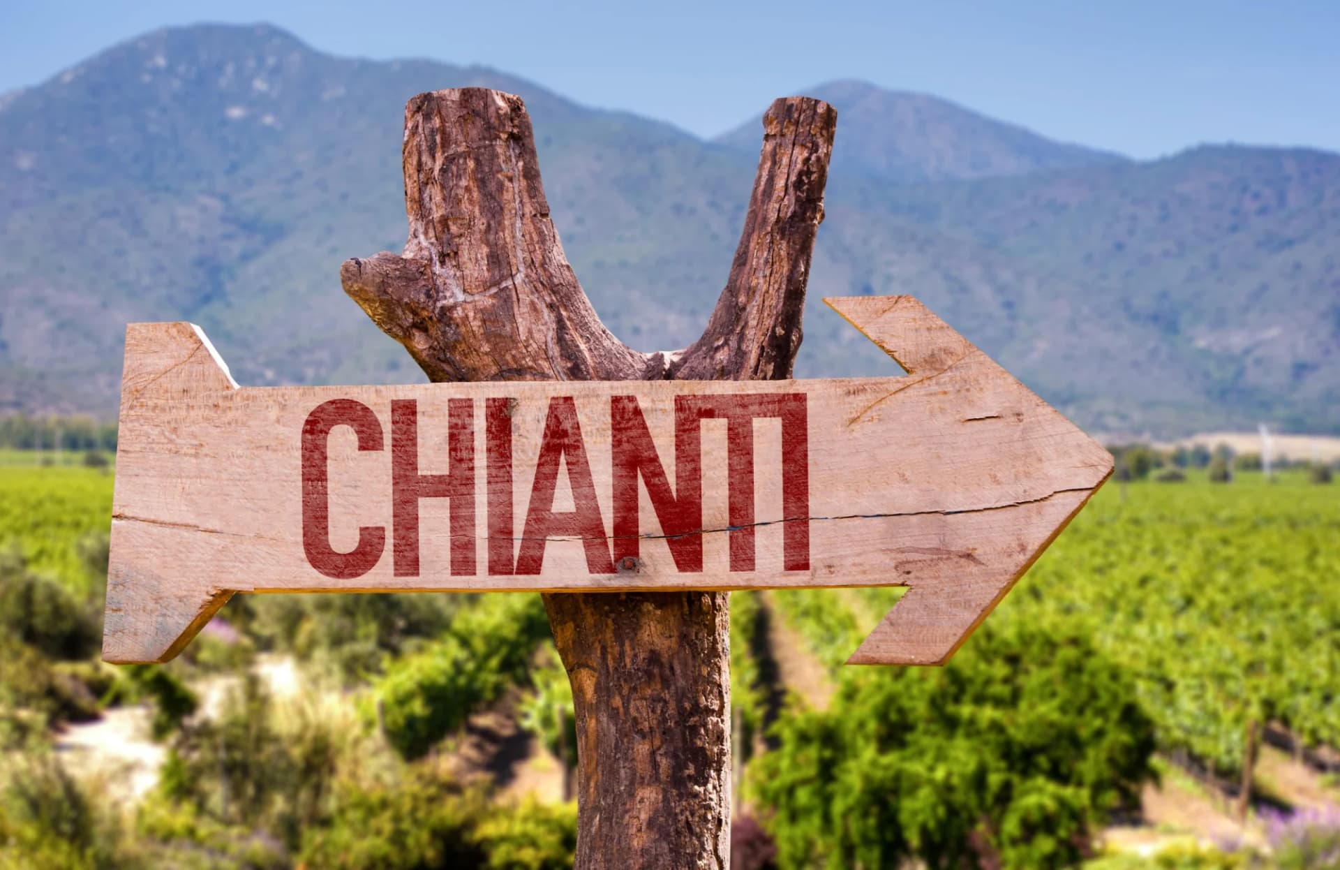 Wooden Chianti wine region sign pointing right over vineyard and mountains