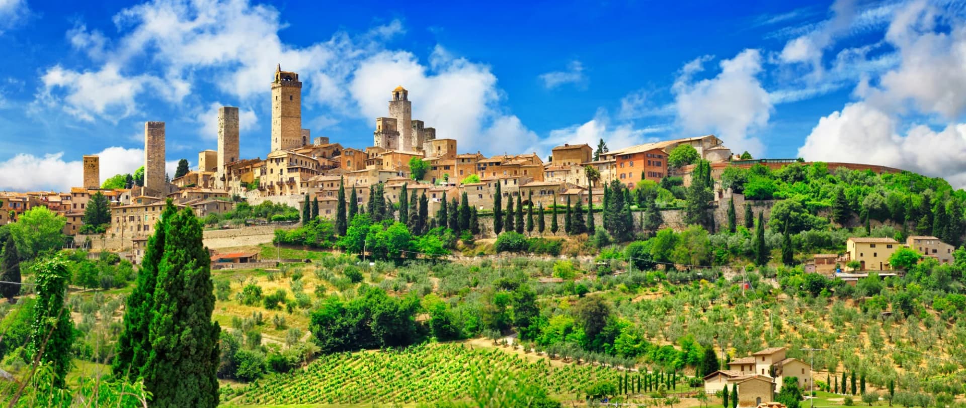 Panorama of San Gimignano Tuscany with medieval towers, vineyards, and cypress trees under blue sky.