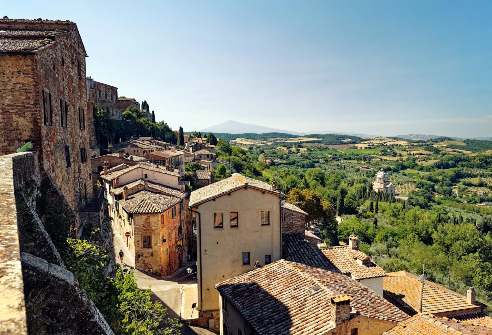 Hilltop town buildings with terracotta roofs overlooking rolling green hills in Montepulciano, Tuscany, Italy.