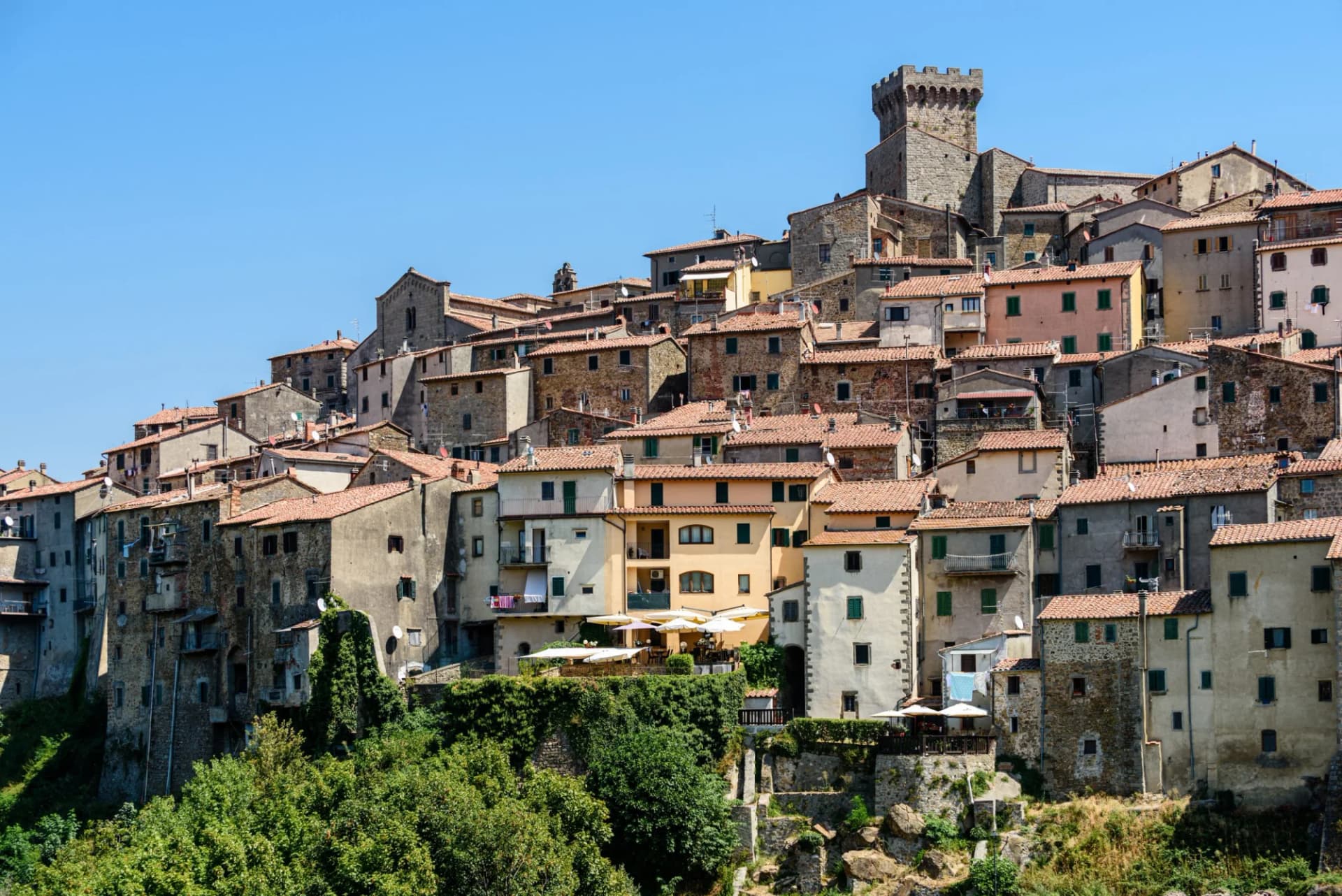 Hillside medieval town with stone tower in Arcidosso, Grosseto, Tuscany under a clear blue sky.