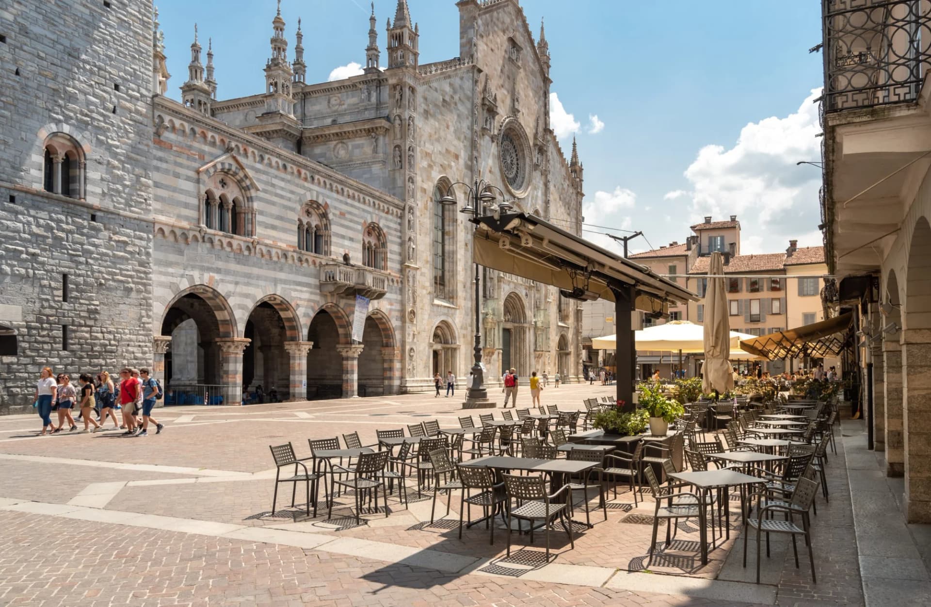 Outdoor cafe tables in piazza next to striped stone cathedral, Como, Italy.