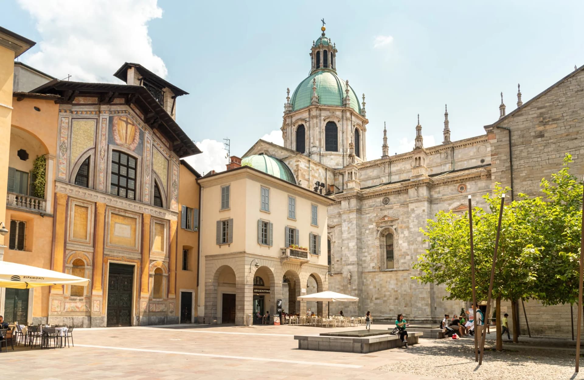 Cathedral with green dome and historic buildings surrounding a sunny piazza in Como, Italy.
