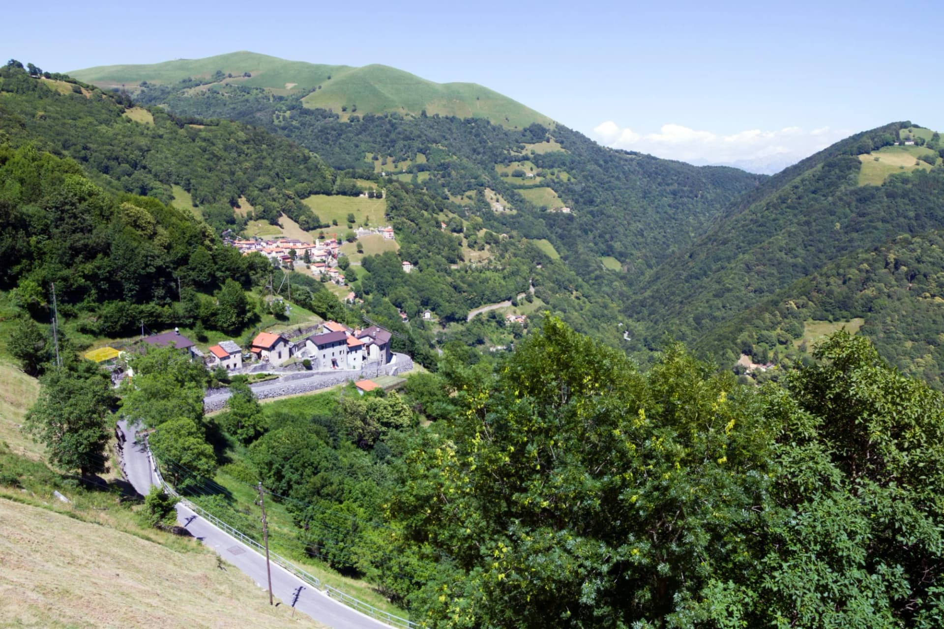 Mountain village nestled in lush green valley with winding road and clear blue sky.