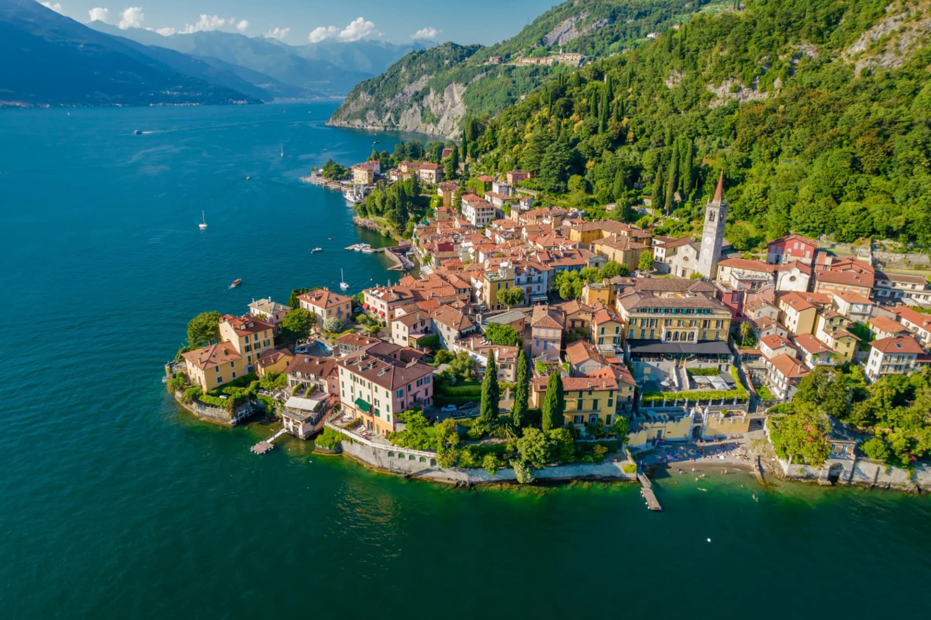 Village on Lake Como with colorful houses, church tower, and steep green mountains.