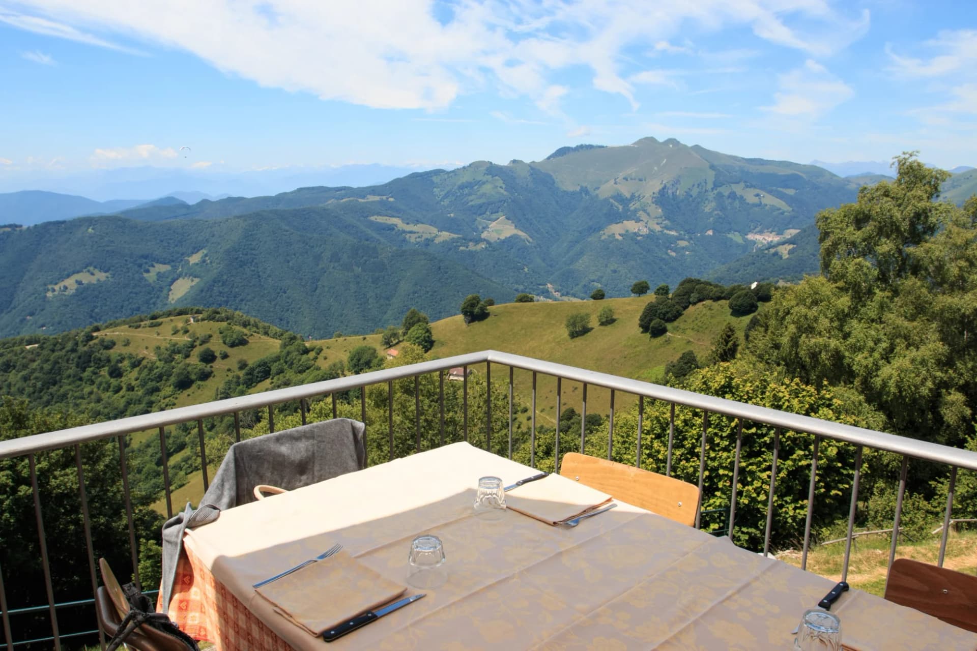 Outdoor dining table overlooking lush green mountains under a blue sky with a paraglider.