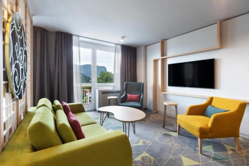Modern hotel living area with lime green sofa, yellow chair, and mountain view balcony.