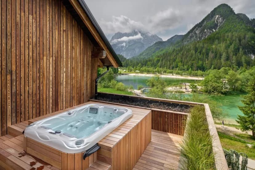 Jacuzzi on wooden deck overlooking green lake and forested mountains, likely Milka Garden Suite.