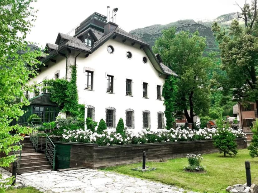 Boutique Hotel Dobra Vila building with white facade, white roses, and green mountains backdrop.