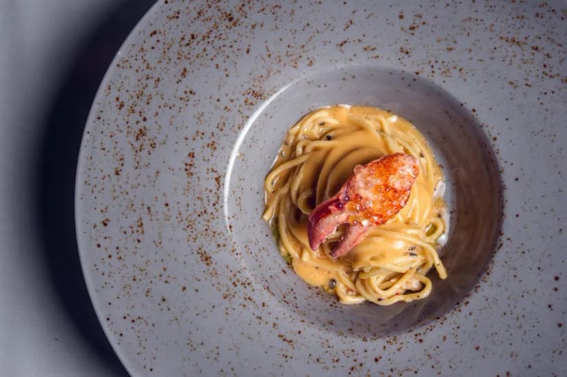 Spaghetti with creamy sauce and lobster claw served in a speckled grey bowl.