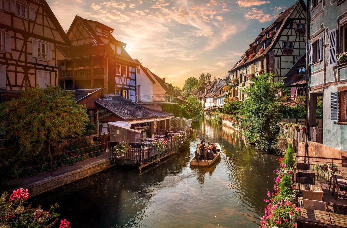 Boat tour on canal past half-timbered houses with outdoor dining in France.