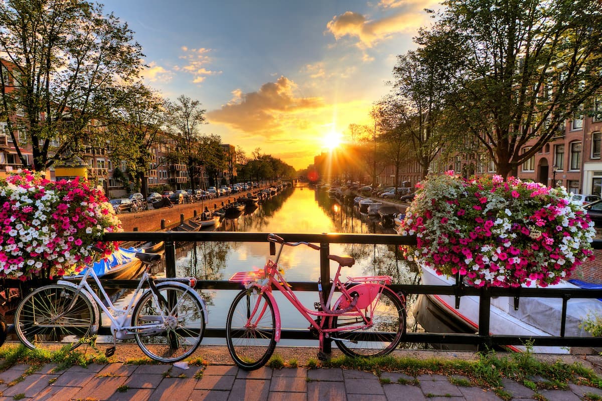 Bicycles parked by canal bridge with flower baskets at sunset in Holland