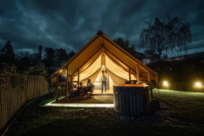 Illuminated glamping tent at night with wooden hot tub and two people near Bled.