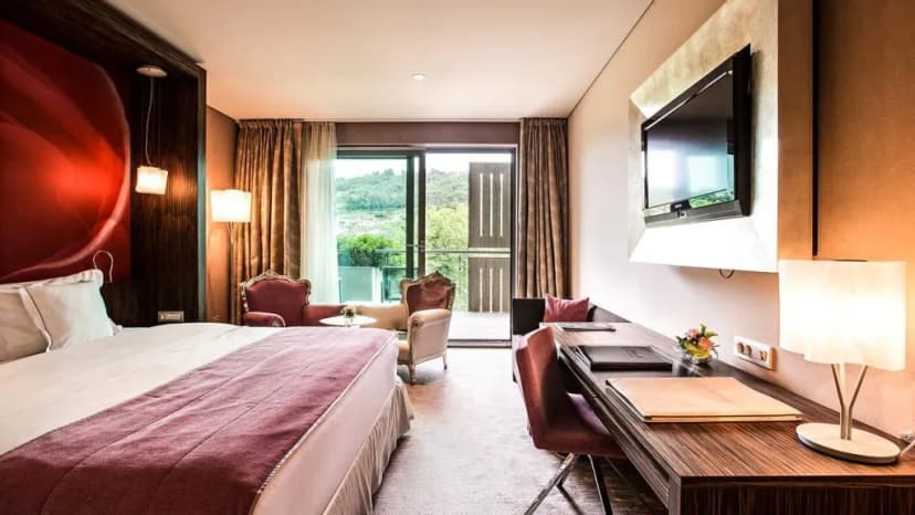 Hotel Kempinski Palace room with large bed, desk, and balcony view of green hills.