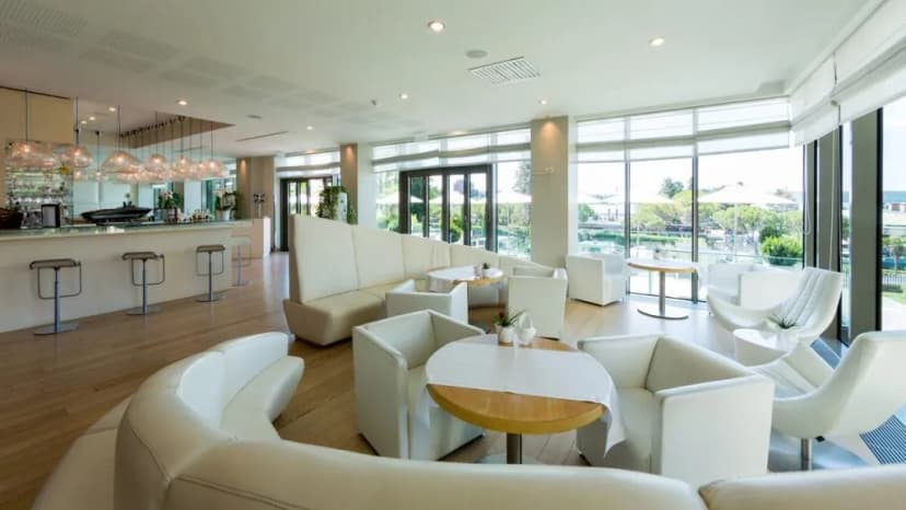 Lobby bar lounge with white modern seating, wood floors, and view of outdoor patio at Hotel Kempinski Palace.