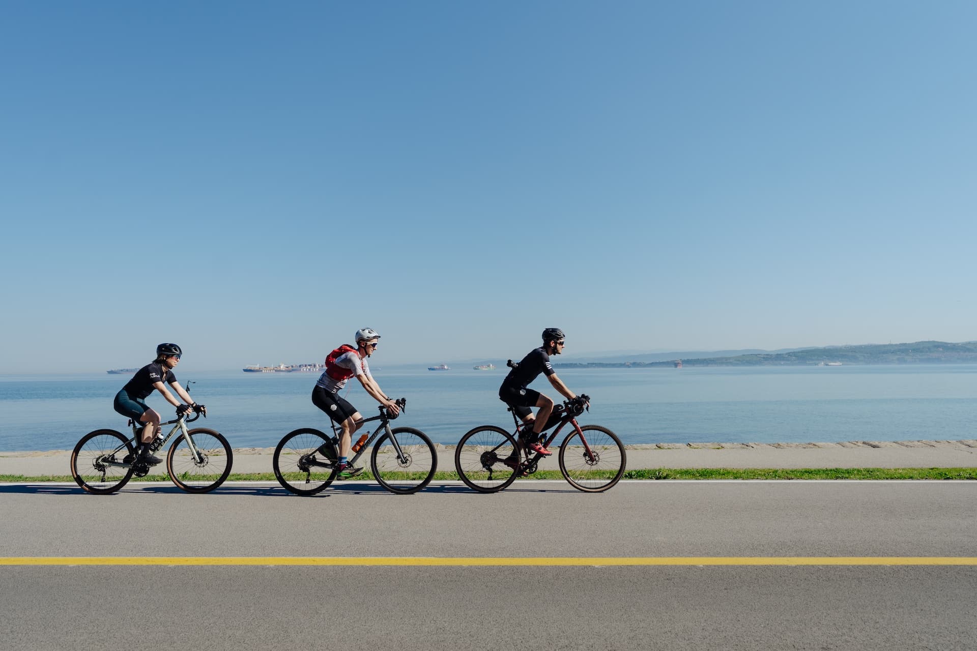 Cyclists riding along the Parenzana Trail by the sea with cargo ships on the water.