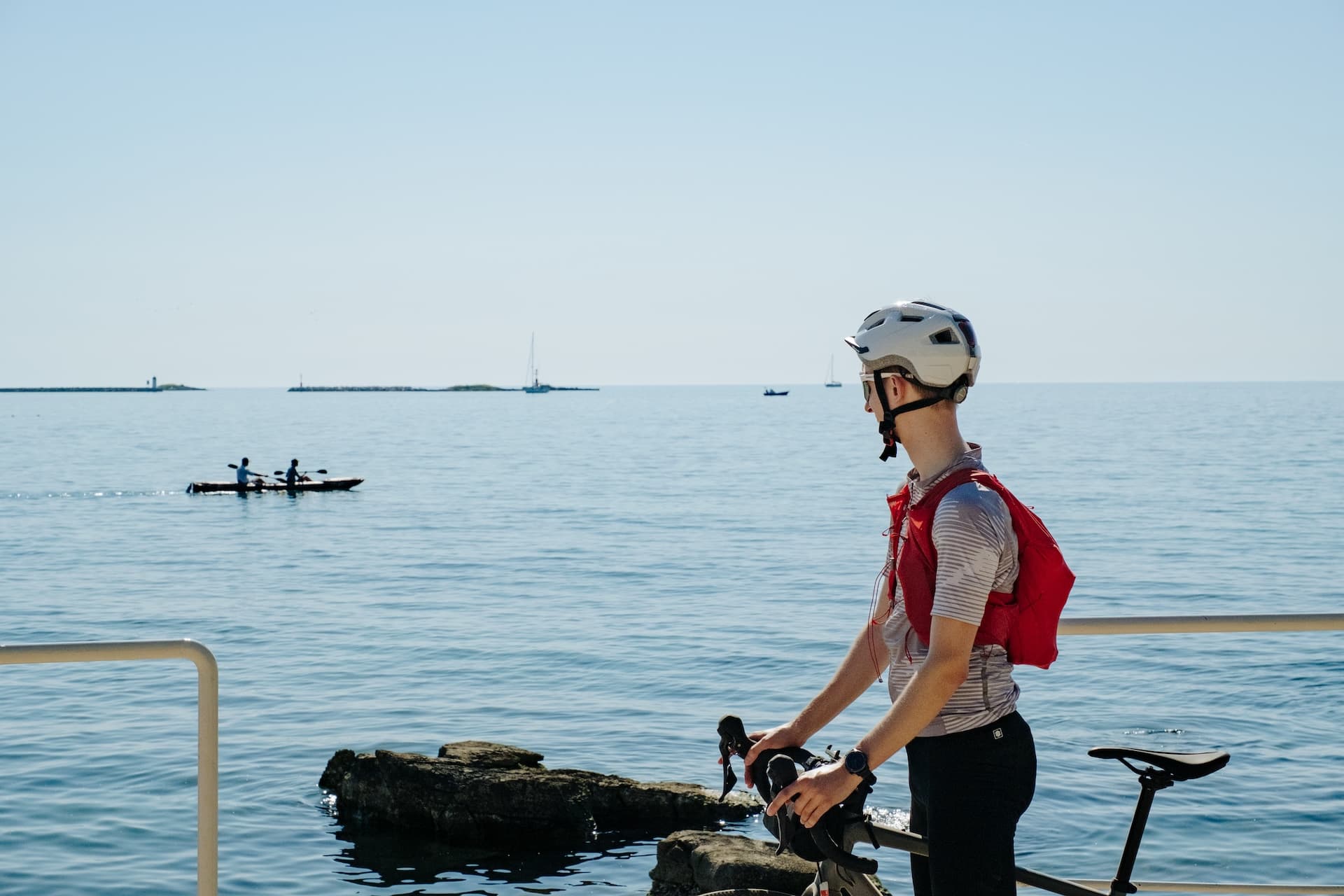 Cyclist taking a break by the sea with kayaks and sailboats on the water