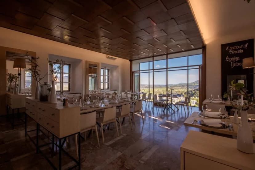 Restaurant dining room with tables set and large windows overlooking a green valley near Bled.
