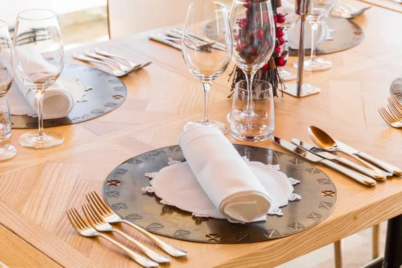 Formal table setting with wine glasses, silverware, and rolled white napkins on a wooden table.