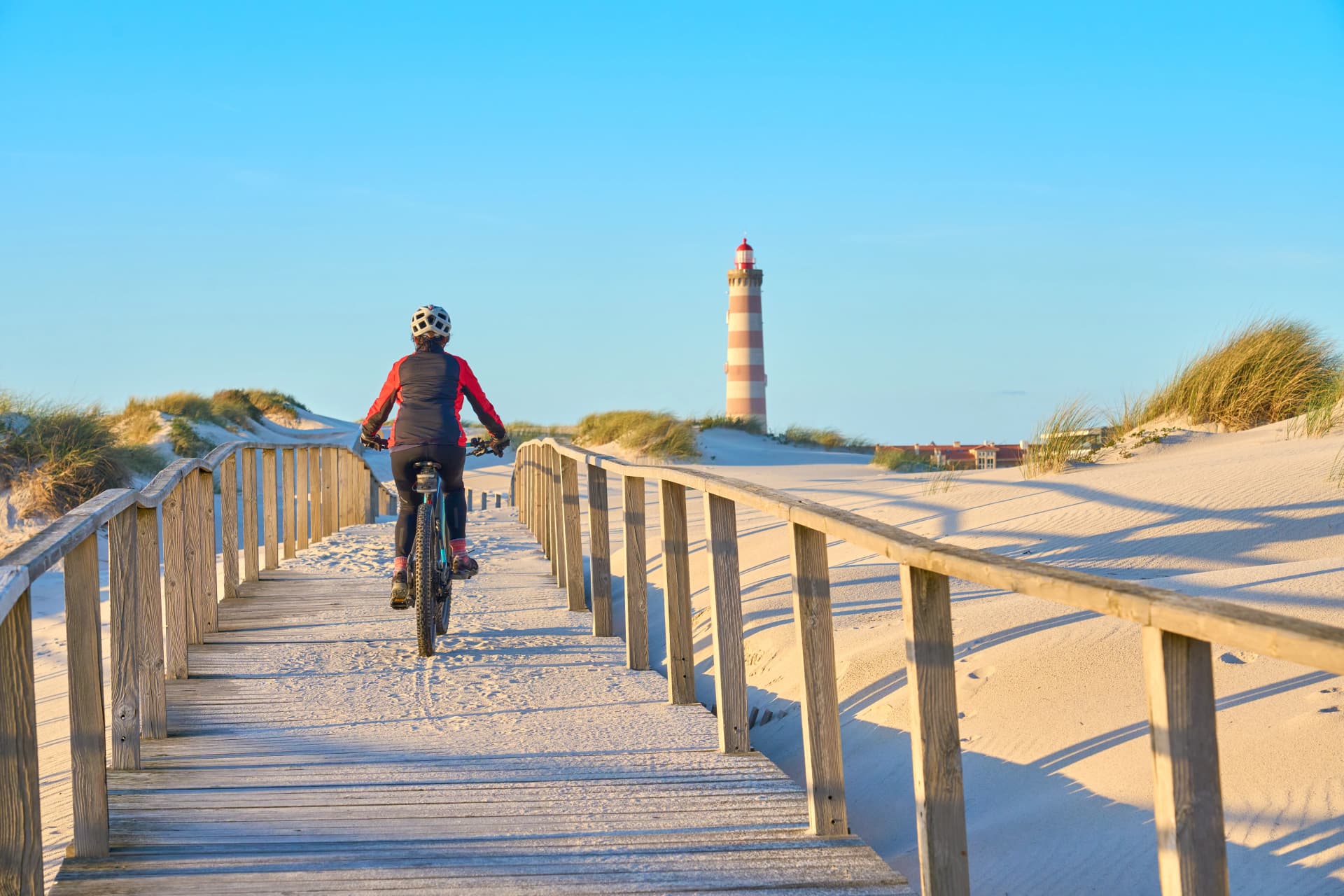 happy active senior woman cycling during moody golden hour at the beach of the atlantic coast below Barra Lighthouse near Aveiro, Portugal Aveiro, Portugal