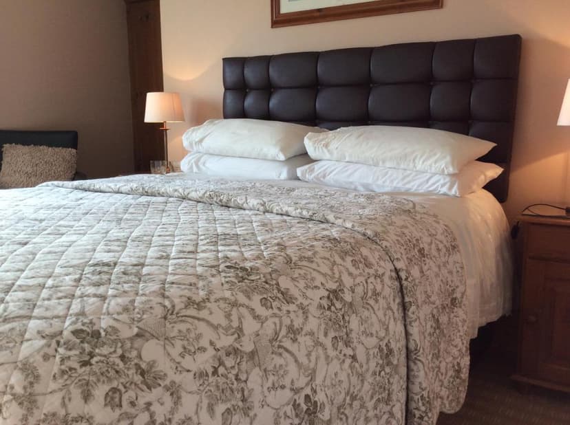 Bedroom with large bed, patterned quilt, white pillows, and dark tufted headboard at Sneem River Lodge B&B.