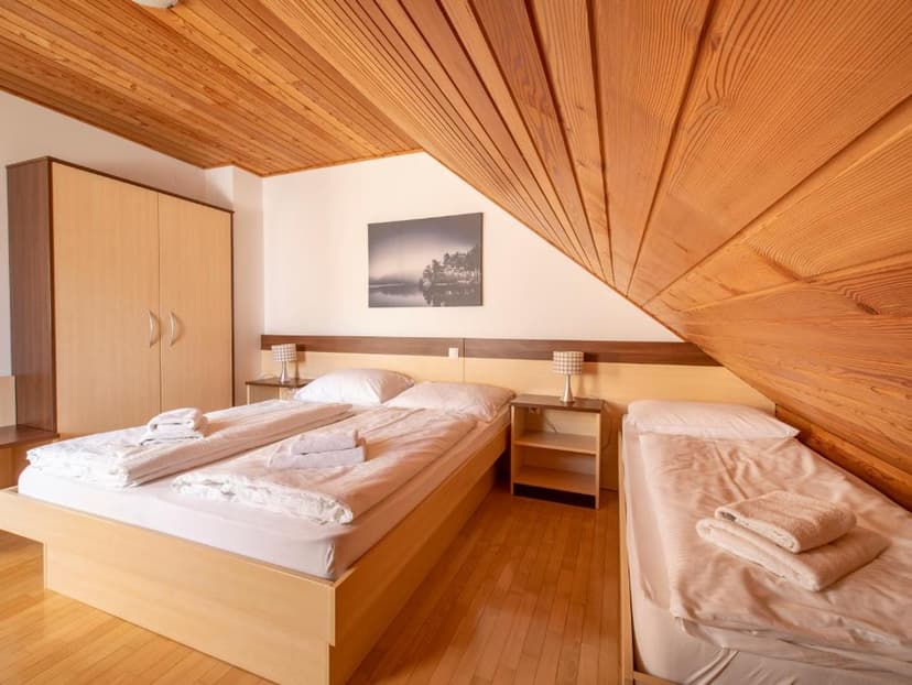 Hotel room with wooden sloped ceiling, two beds with white linens, and light wood furniture